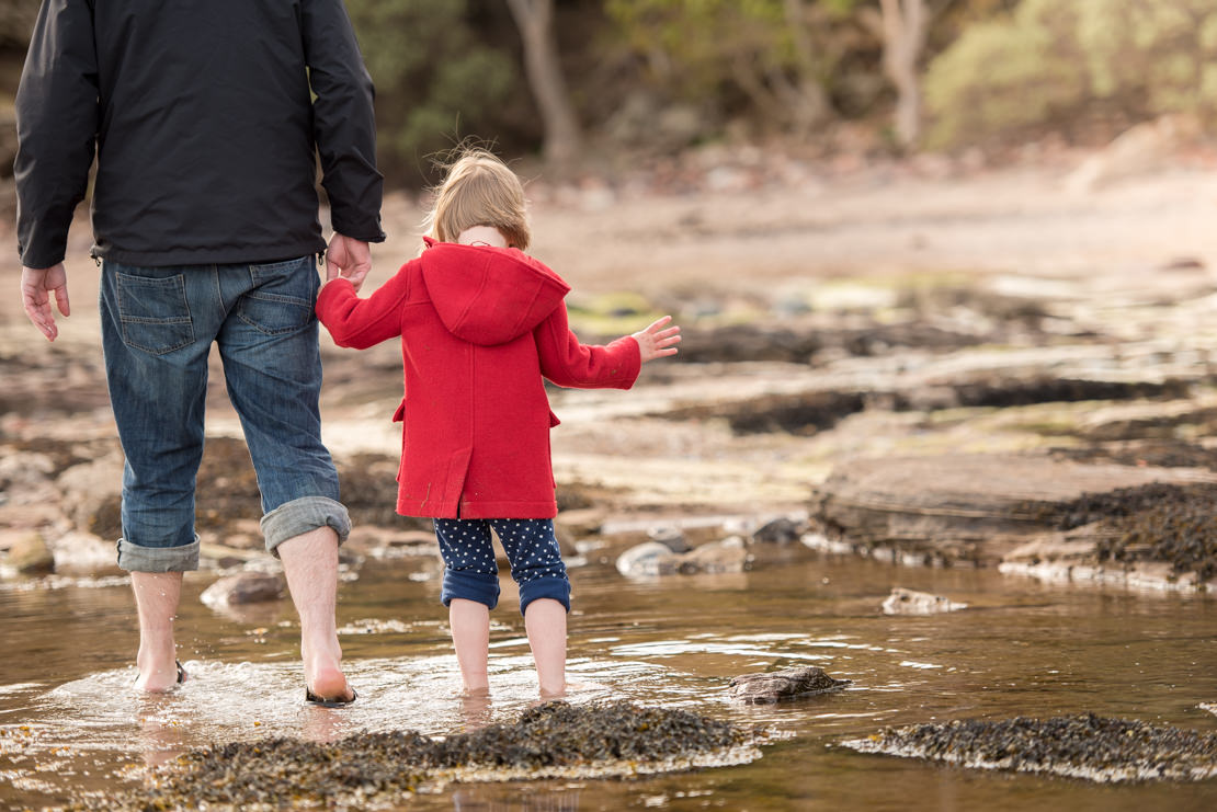 little girl walking with daddy through rock pool 