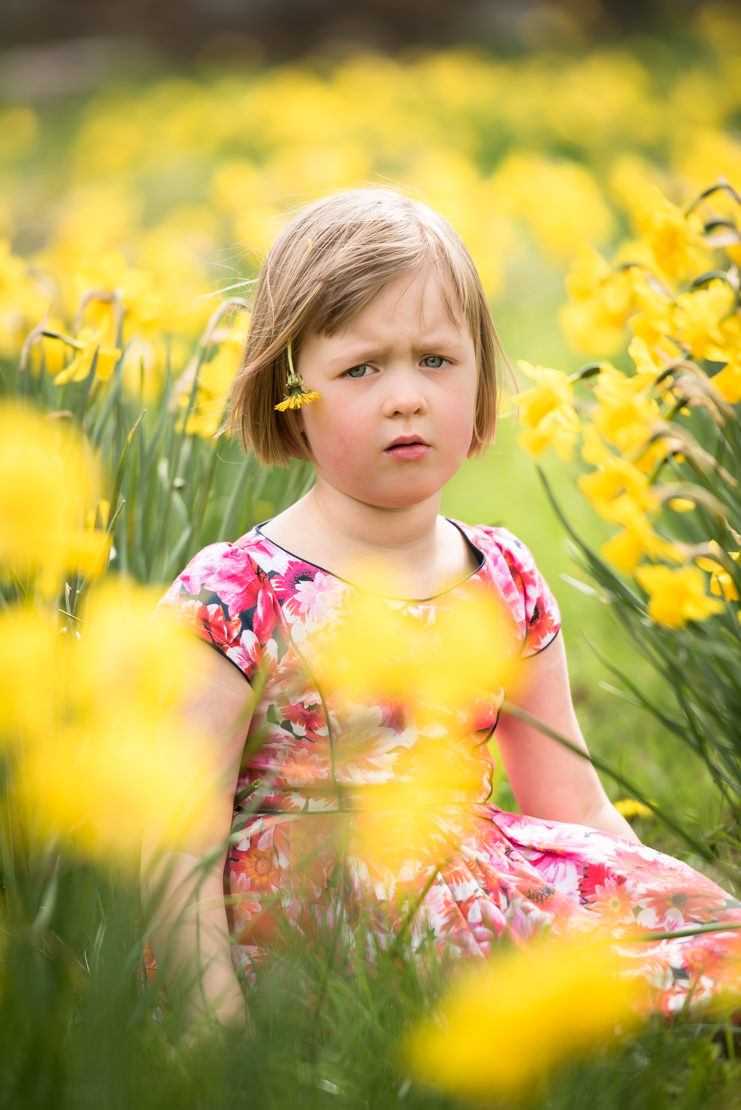 how to get your children to smile in photographs - little girl sitting in field of daffodils frowning