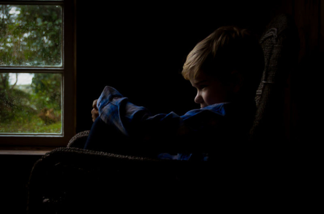 Family photographer Edinburgh - little blonde haired boy in profile sitting in window, back lit