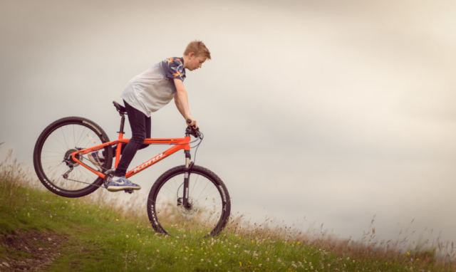 Family photographer Edinburgh - 13 year old boy on mountain bike cycling downhill in a field of flowers