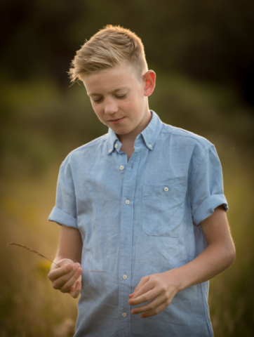 Family photographer Edinburgh - 12 year old boy with blonde hair in a blue shirt in a cornfield, holding a corn stalk