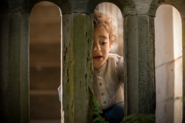 Family photographer Edinburgh - little boy with brown eyes and brown curly hair peeking through stone banisters