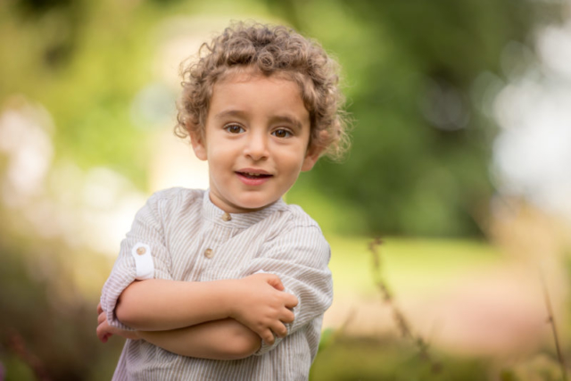 Family photographer Edinburgh - 2 year old boy with brown eyes and brown curly hair crossing his arms and smiling