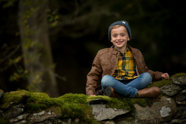 Family photographer Edinburgh - little boy with bright yellow tartan shirt sitting cross legged on a dry stone wall