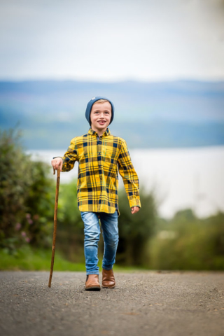 Family photographer Edinburgh - little boy with bright yellow tartan shirt and shepherd's crook waking along road