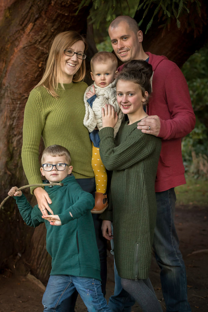 Family photographer Edinburgh - family group of mum, dad, two sisters and brother, standing against a tree