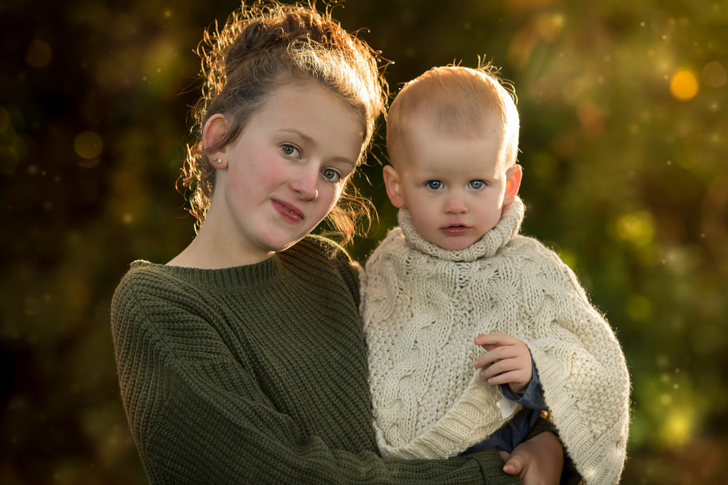 Family photographer Edinburgh - big sister holding little toddler sister in the evening sunshine