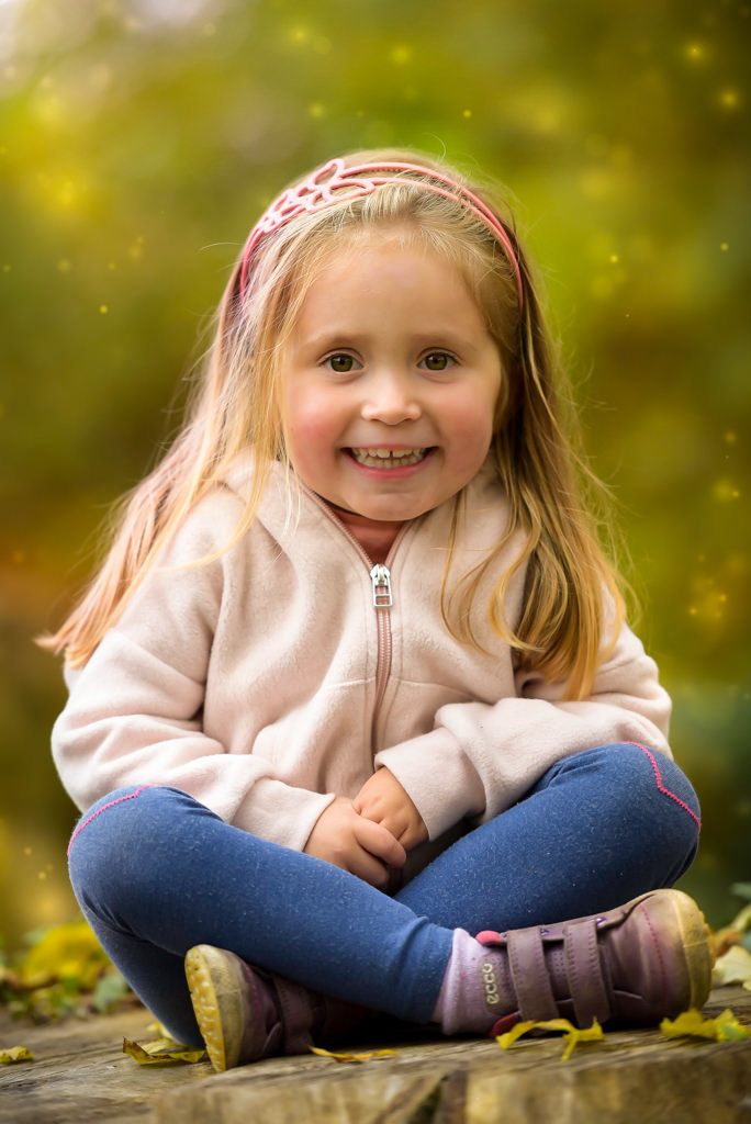 Family photographer Edinburgh - little girl with brown eyes and blonde hair sitting cross legged and smiling