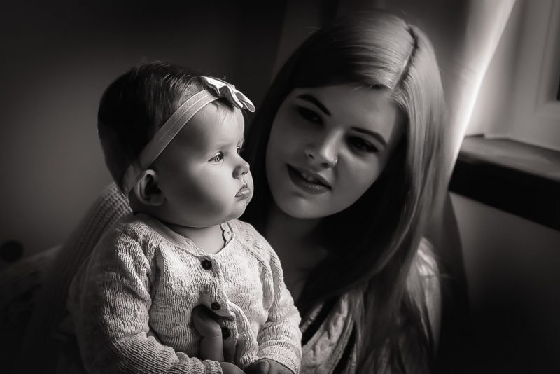 Family photographer Edinburgh - black and white photo of baby in headband sitting on mother's knee in window light