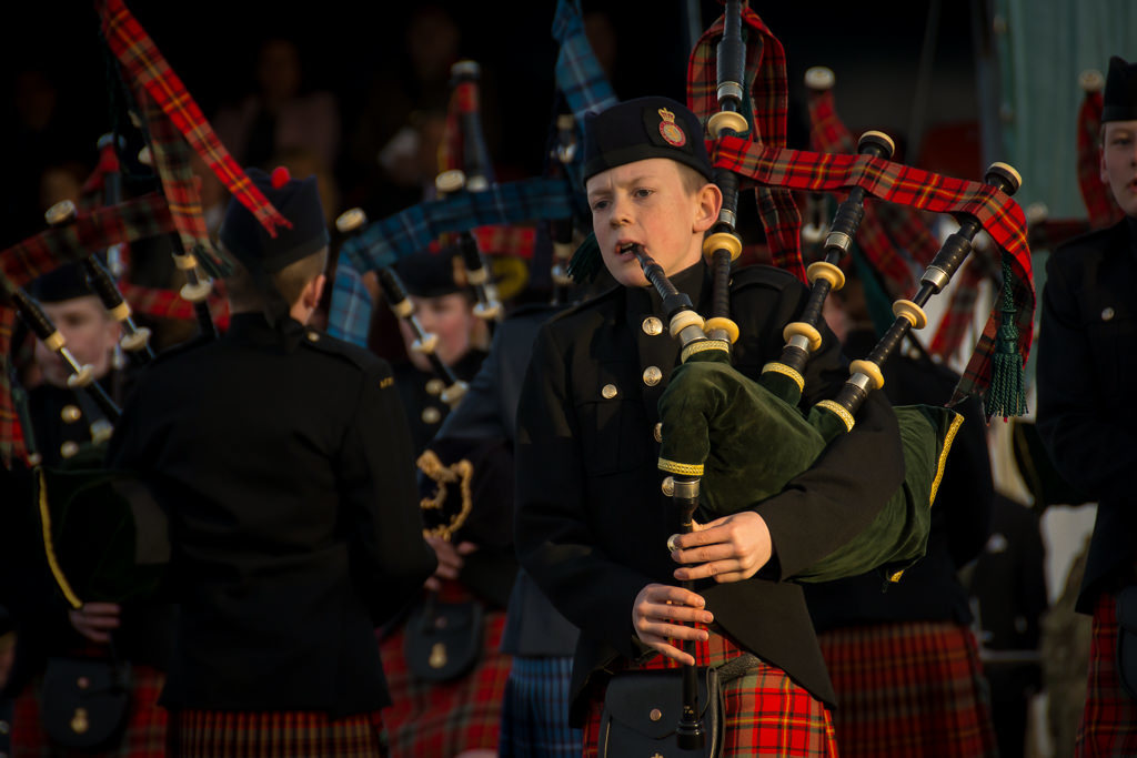 Family photography in Edinburgh of 13 year old boy playing the bagpipes at Edinburgh Castle in red tartan Army Cadet kilt uniform