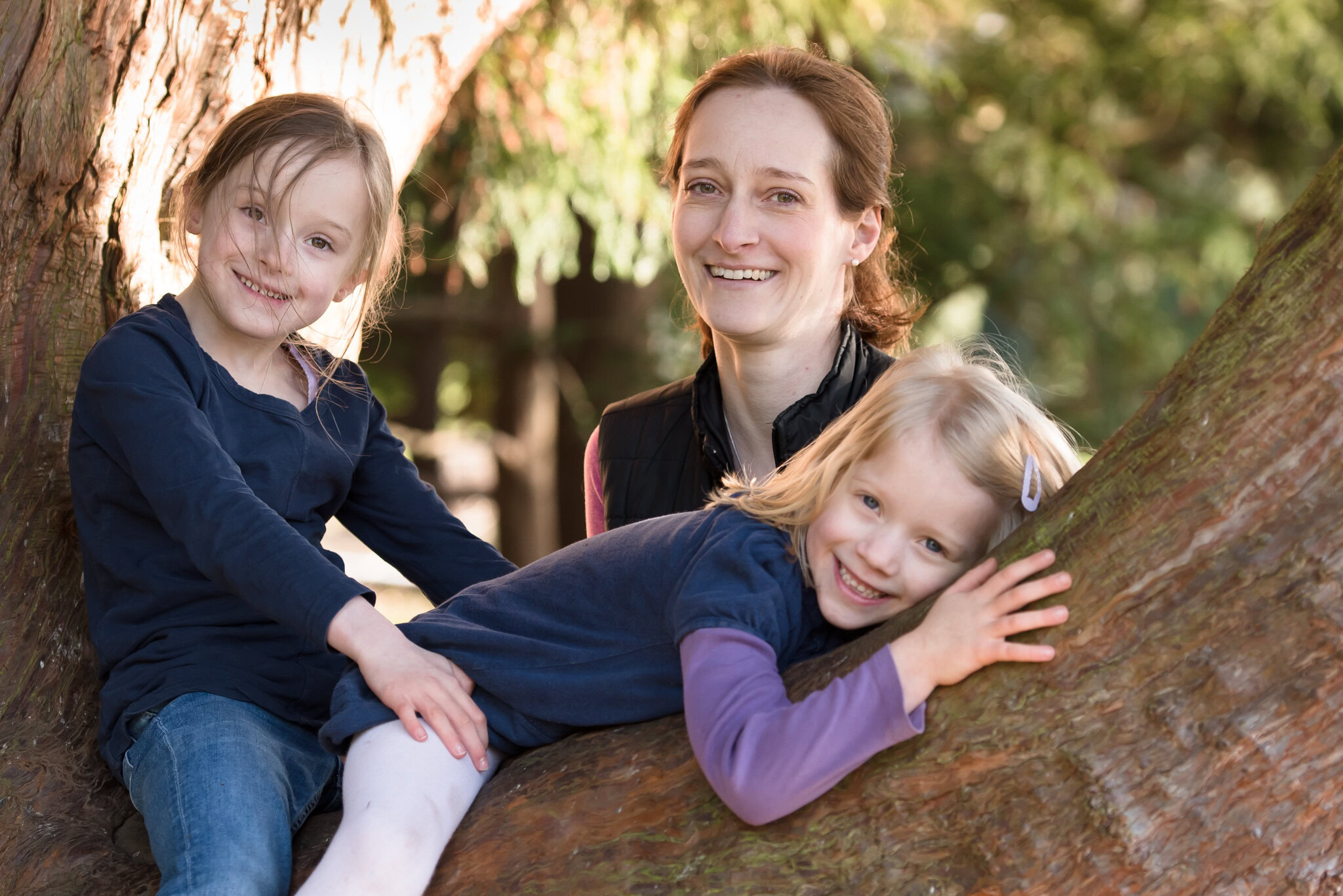 Family photographer Edinburgh - mother standing behind two little daughters in a tree