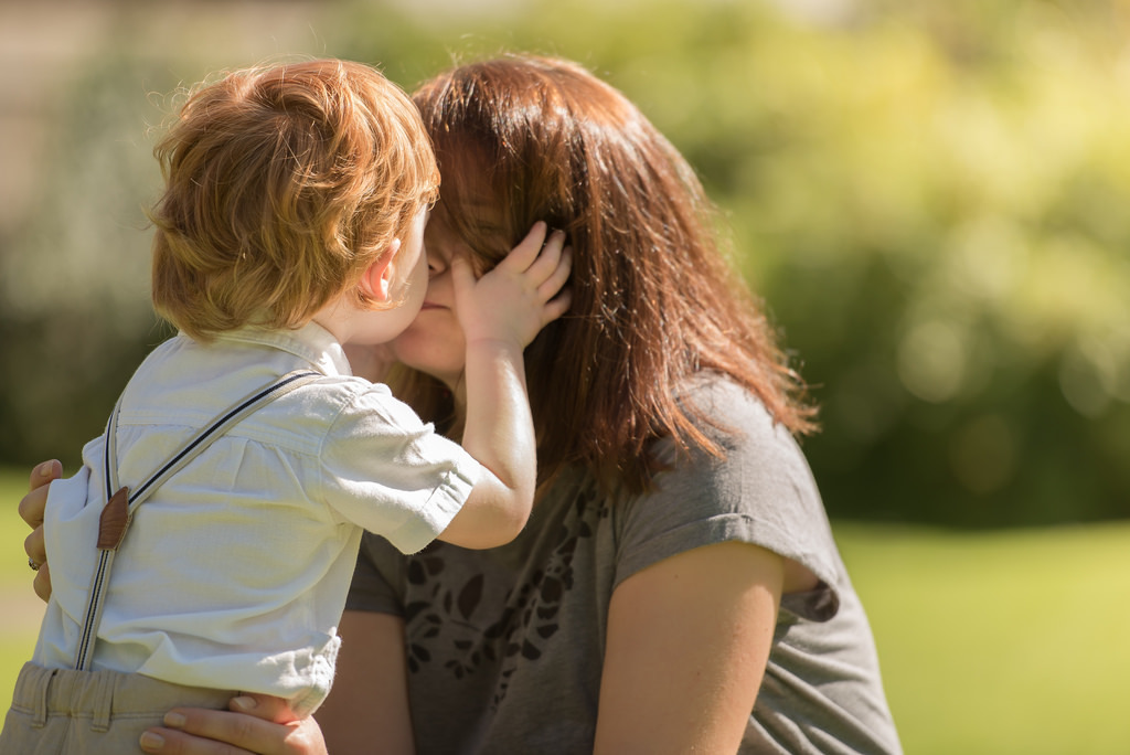 Family photographer Edinburgh - 2 year old boy with bright red hair kissing his mother in the evening sunshine