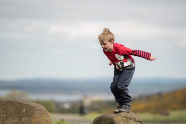 Small boy in red top jumping from a rock up Calton Hill in Edinburgh