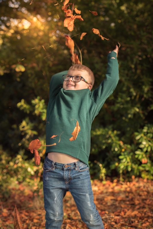 little boy throwing autum leaves in the air