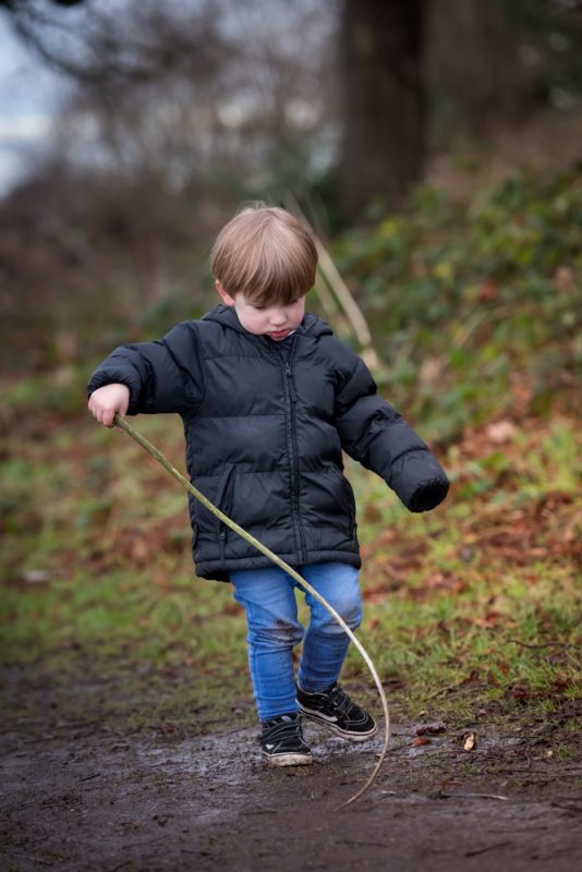 little boy with stick poking in a puddle