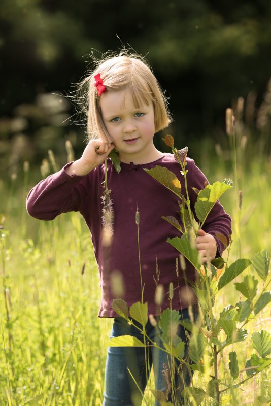 sunset photography sessions - Edinburgh Portrait Photographer - little blonde haired girl wearing purple top in a grassy field, backlit