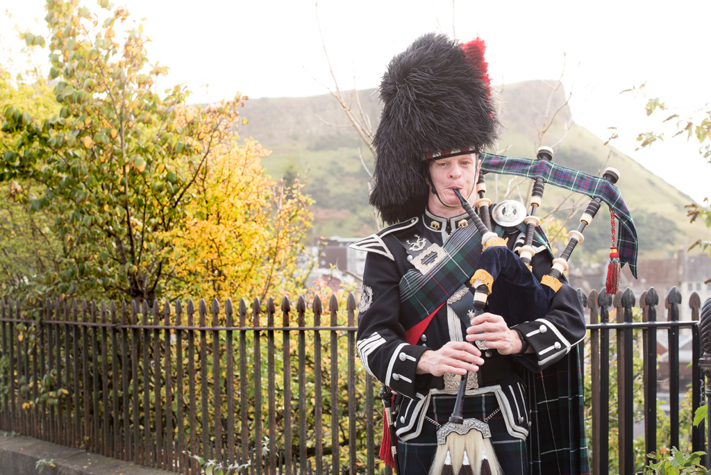 Scottishbagpipers.com - Piper in full highland dress standing in front of Salisbury Crags
