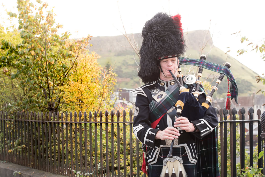 Scottishbagpipers.com - Piper in full highland dress standing in front of Salisbury Crags