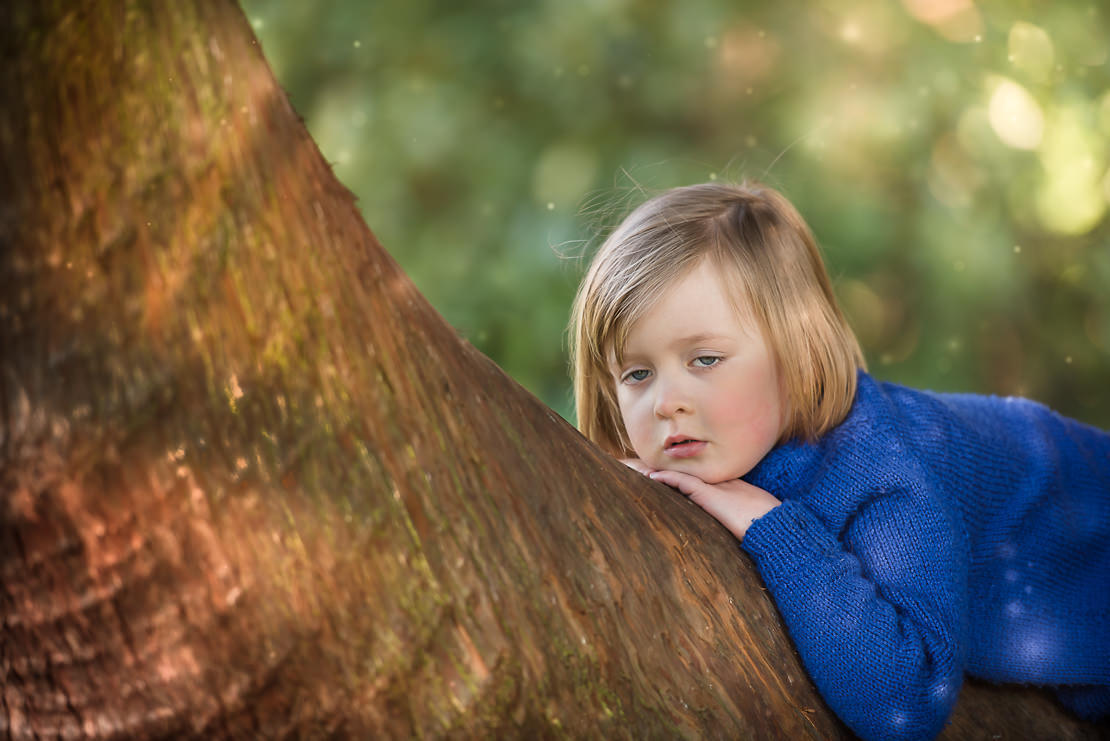 Family photographer Edinburgh - small girl lying in a tree looking bored