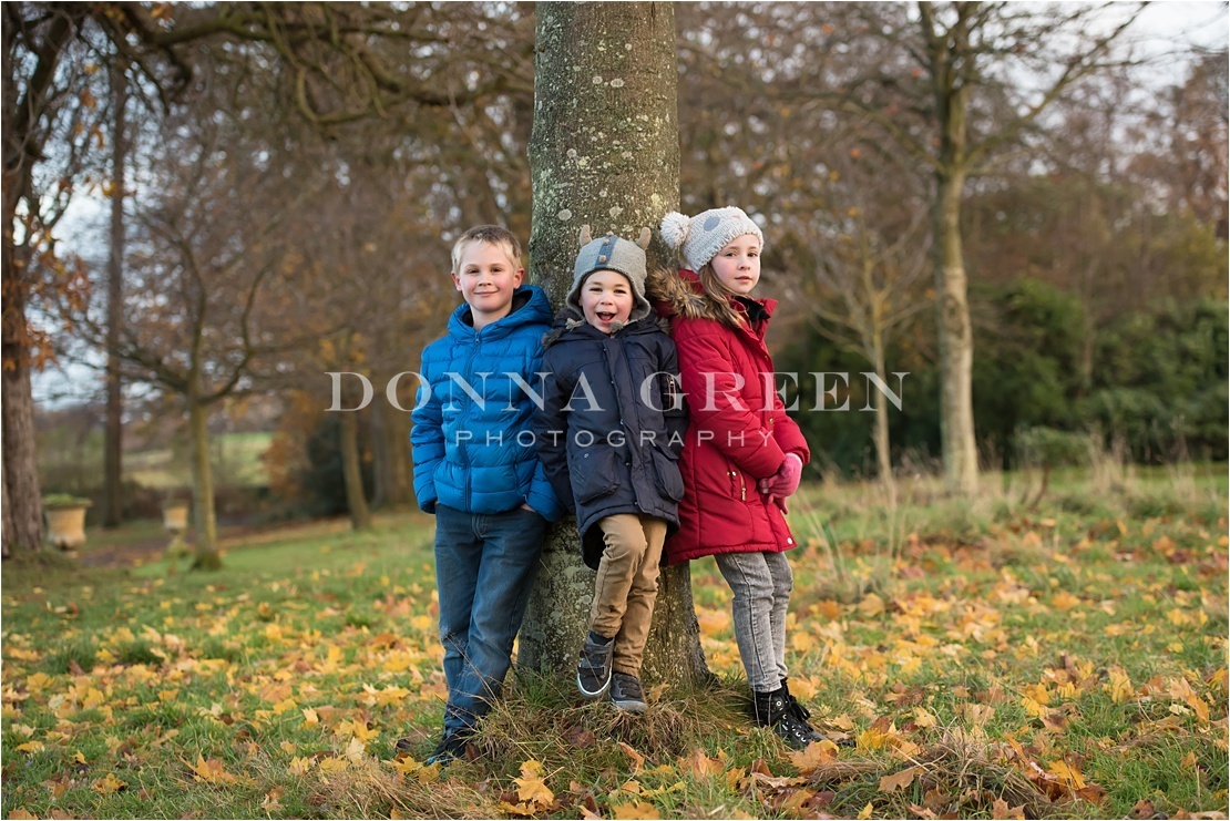 Family photo shoot in Edinburgh - two little boys and girl standing against a tree with autumn leaves