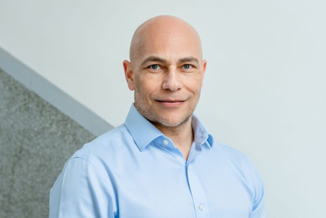 Headshot in Edinburgh, Scotland, of bald-headed man with blue eyes wearing a light blue shirt against a grey wall