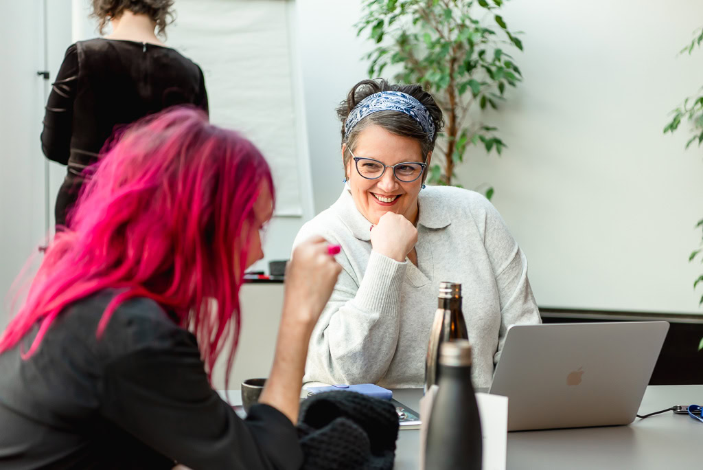 Branding photo shoot in Edinburgh Scotland for women business owners - woman at laptop talking to another woman with pink hair