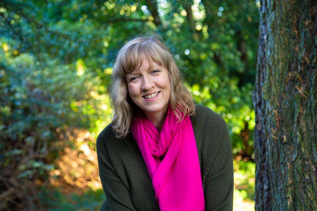 Brand photographer headshot in Edinburgh Scotland of woman with pink scarf sitting on tree branch in woods