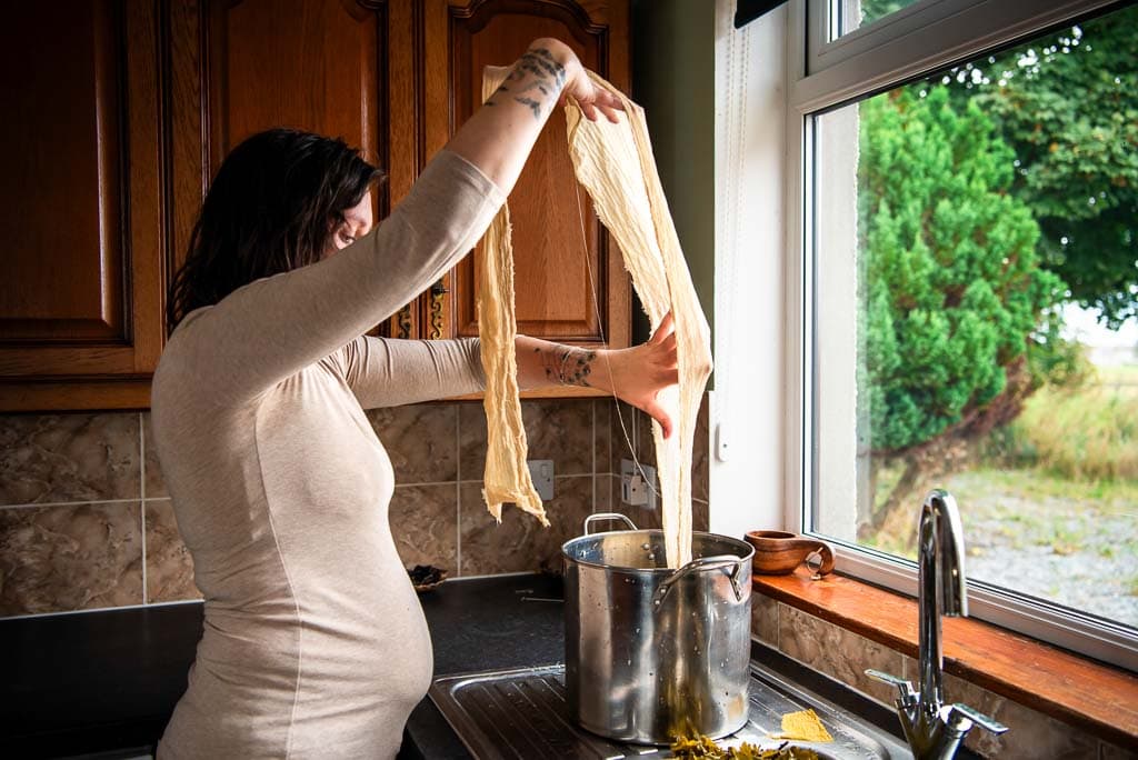 Heritage craftswoman examining material steeped in natural dye made in her kitchen on the Moray coast, an image designed to show the value of your work, photographed by a brand photographer in Scotland.