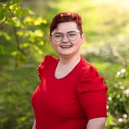 Rachael-Davis-Headshot Woman in red top against yellow background